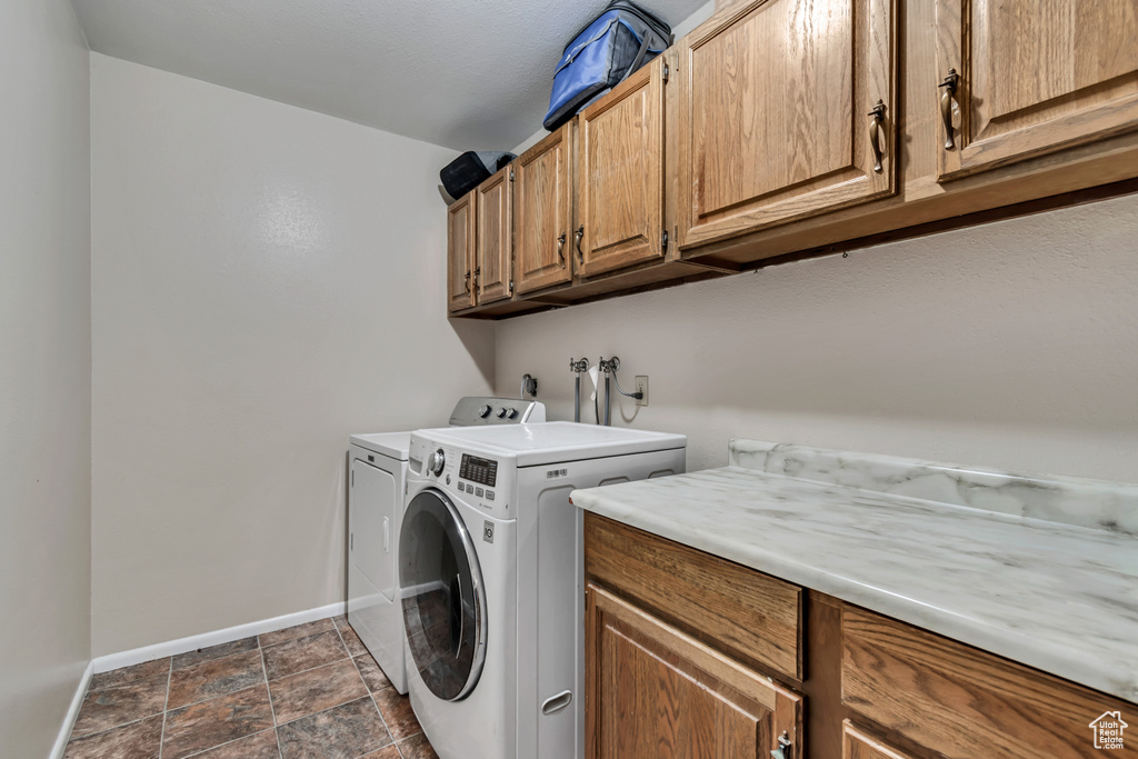 Laundry room featuring separate washer and dryer, cabinet space, baseboards, and stone finish floor
