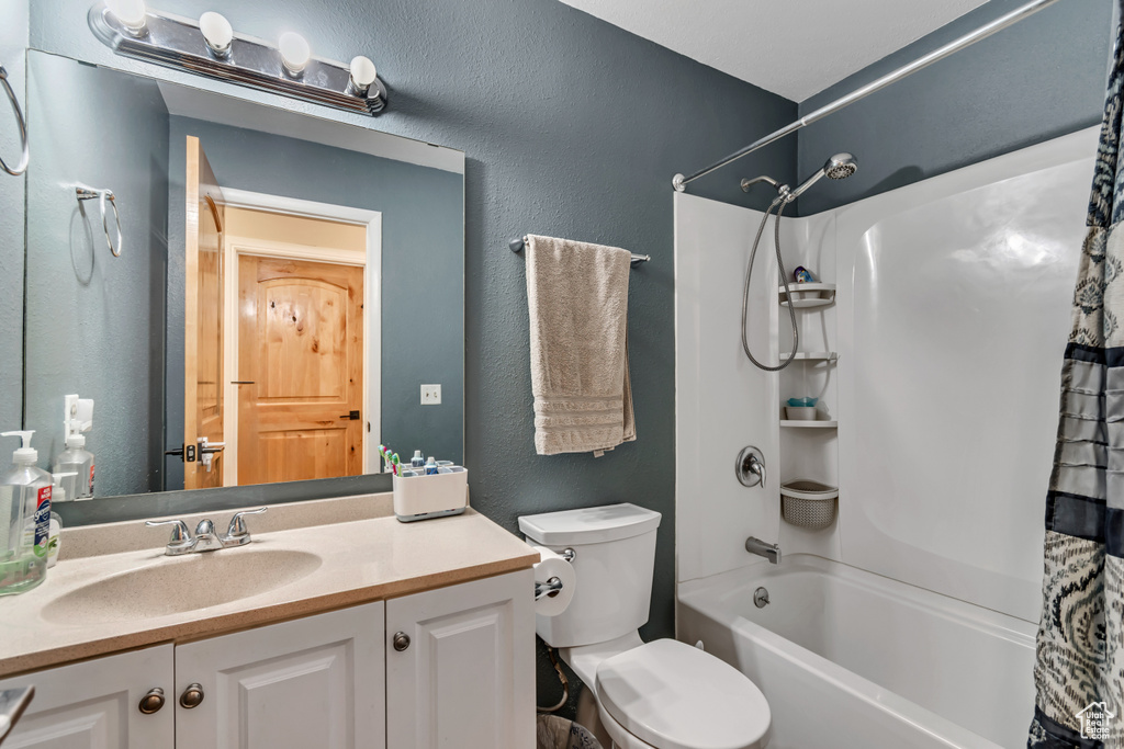 Full bath featuring toilet, a textured wall, shower / bathtub combination with curtain, and vanity