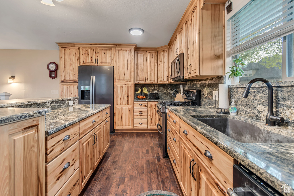 Kitchen featuring dark wood-style flooring, a sink, dark stone countertops, light brown cabinets, and stainless steel appliances
