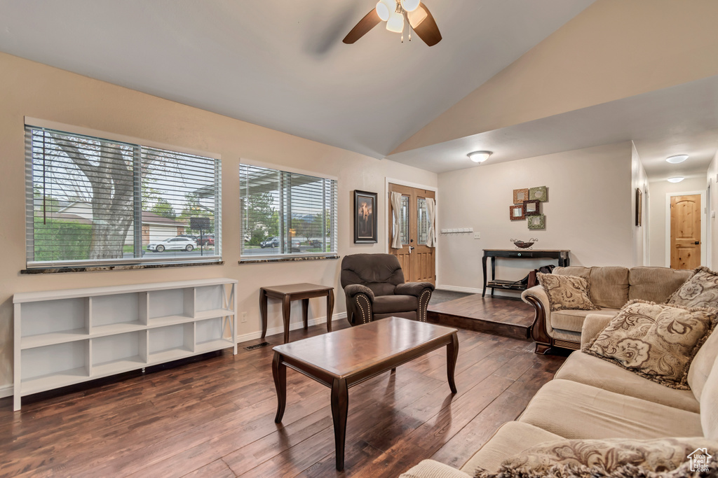 Living room with baseboards, ceiling fan, vaulted ceiling, and dark wood-type flooring