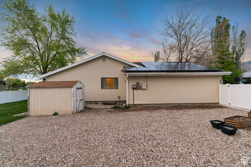 Back of house at dusk featuring an outbuilding, solar panels, a fenced backyard, and a storage unit