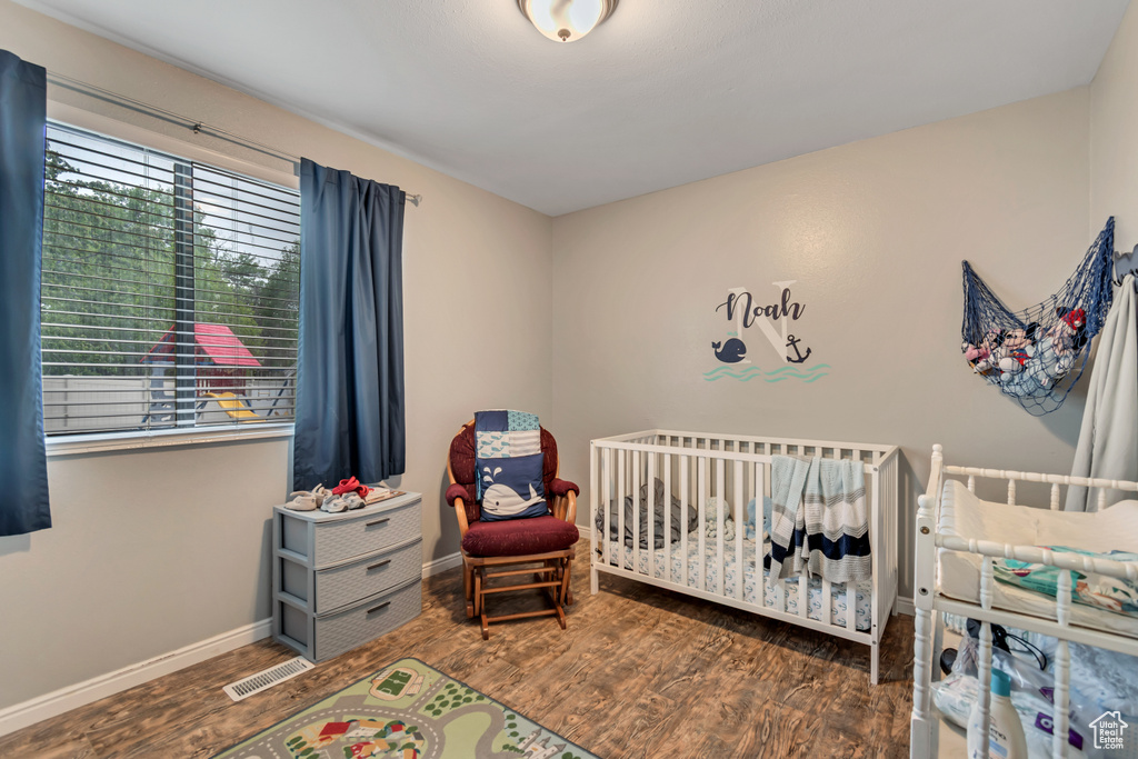 Bedroom featuring baseboards, a crib, wood finished floors, and visible vents