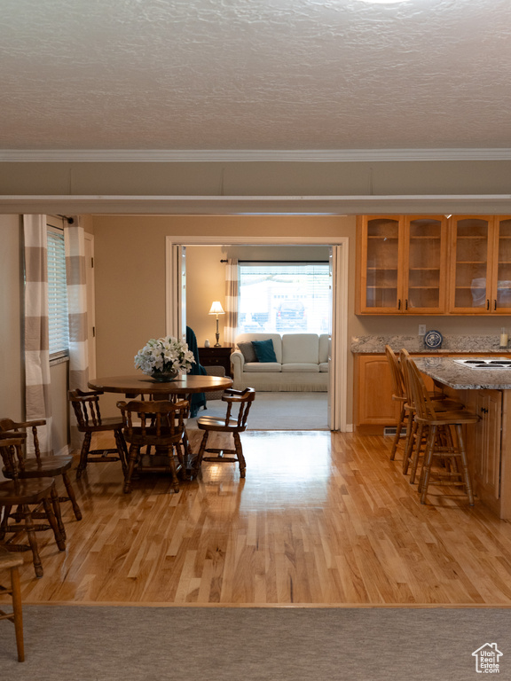 Dining space with crown molding, a textured ceiling, and light wood-type flooring