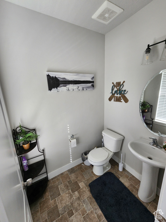 Half bathroom with stone finish flooring, visible vents, a sink, baseboards, and toilet