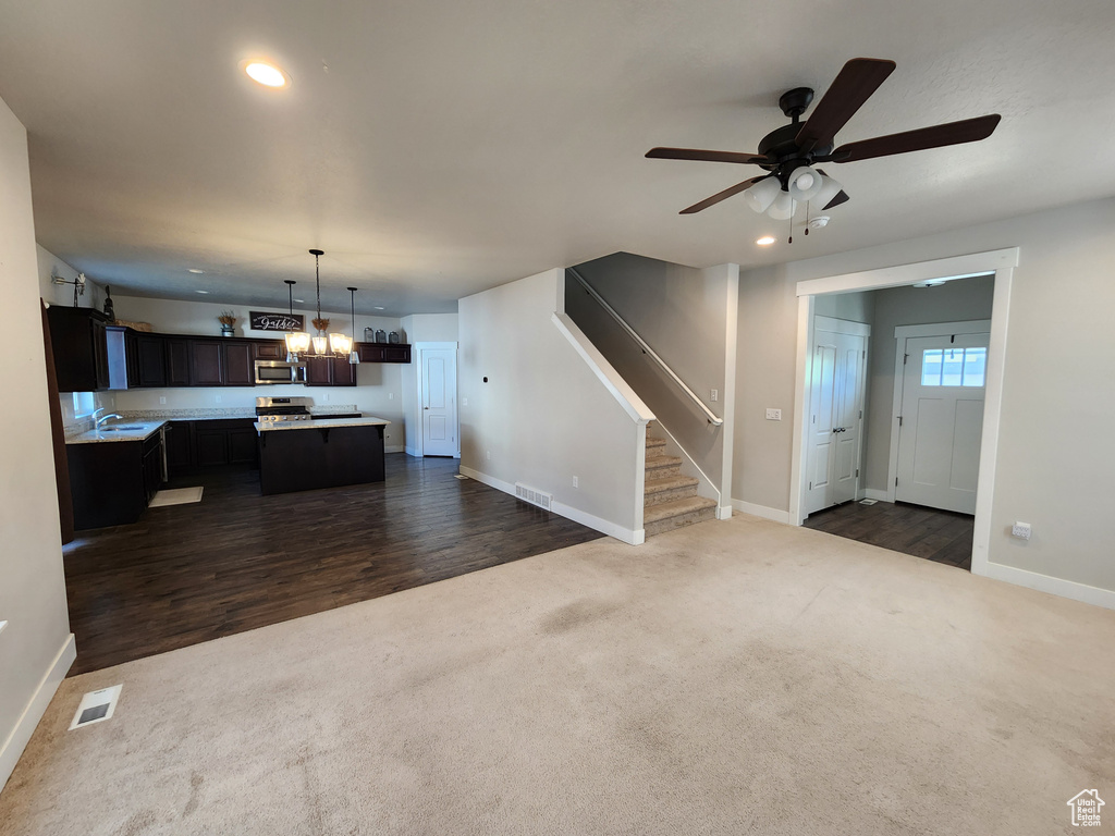 Unfurnished living room featuring dark colored carpet, baseboards, ceiling fan with notable chandelier, and visible vents