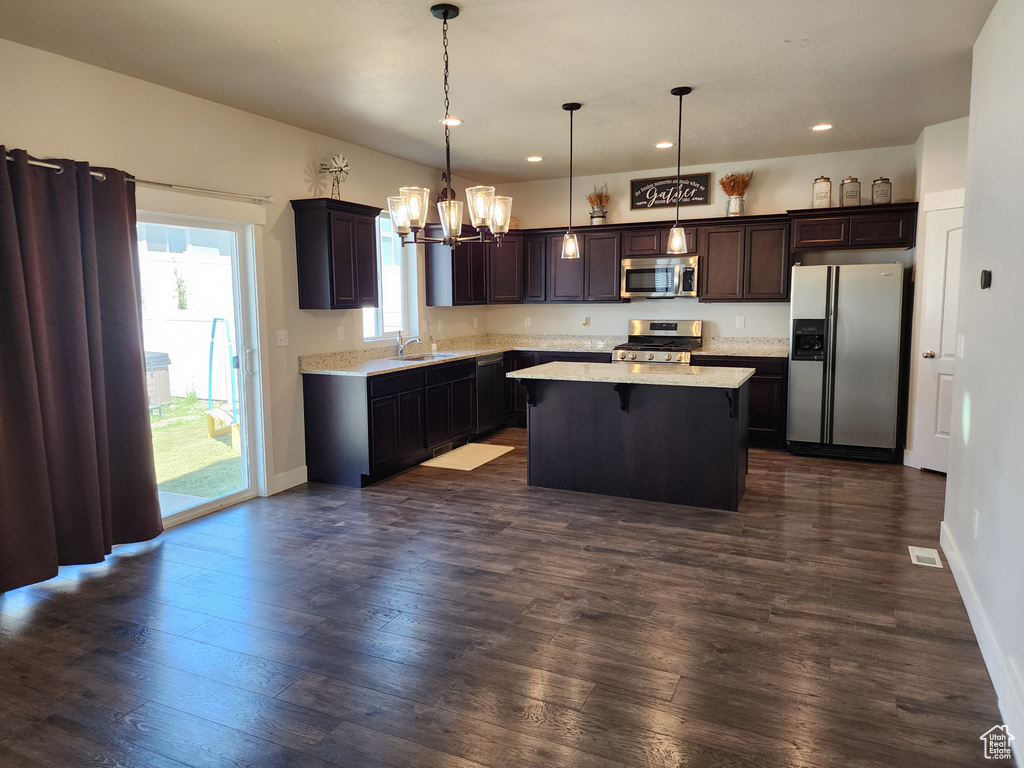 Kitchen featuring appliances with stainless steel finishes, a sink, a chandelier, a kitchen island, and dark brown cabinetry