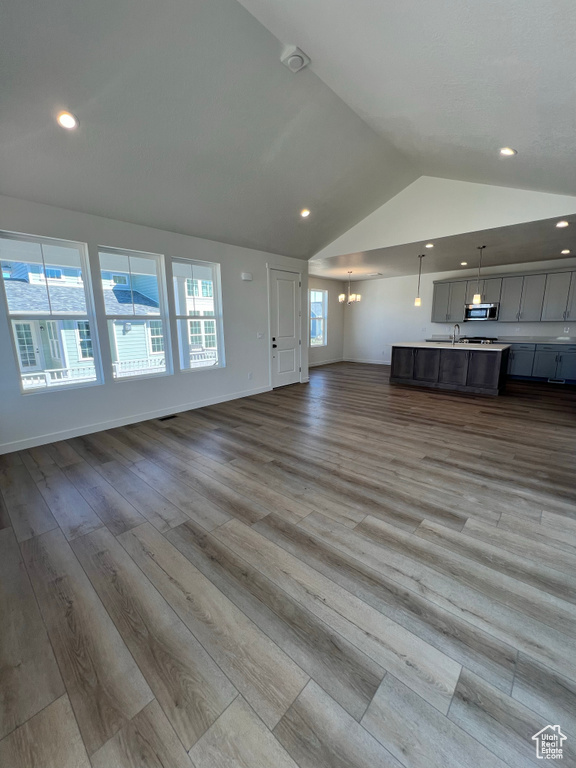 Unfurnished living room featuring an inviting chandelier, plenty of natural light, wood finished floors, and lofted ceiling