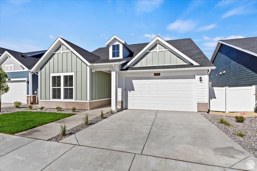 View of front facade featuring a garage, brick siding, a shingled roof, board and batten siding, and driveway