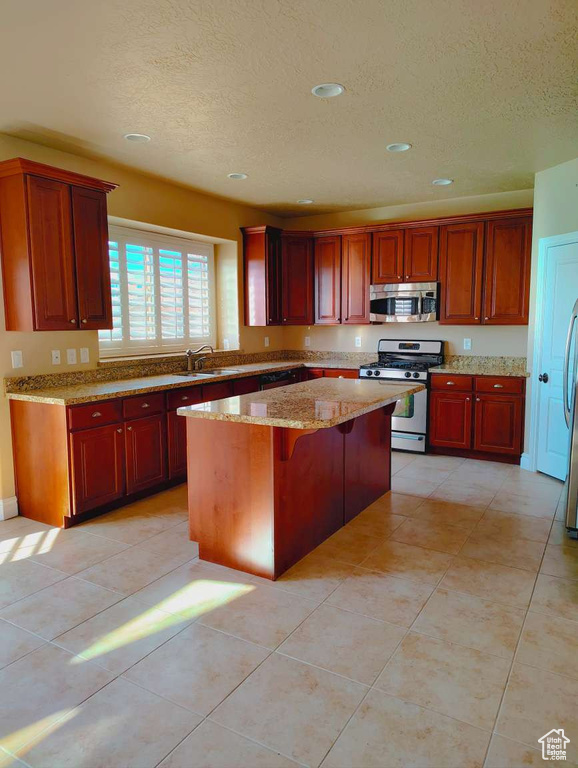 Kitchen with light stone countertops, appliances with stainless steel finishes, a textured ceiling, recessed lighting, and a kitchen island