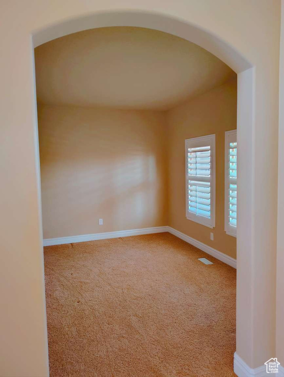 Spare room featuring carpet floors, arched walkways, baseboards, and visible vents