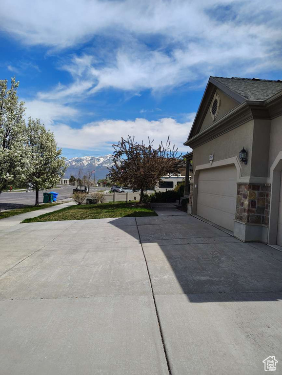 View of home's exterior featuring an attached garage, stone siding, stucco siding, a mountain view, and driveway
