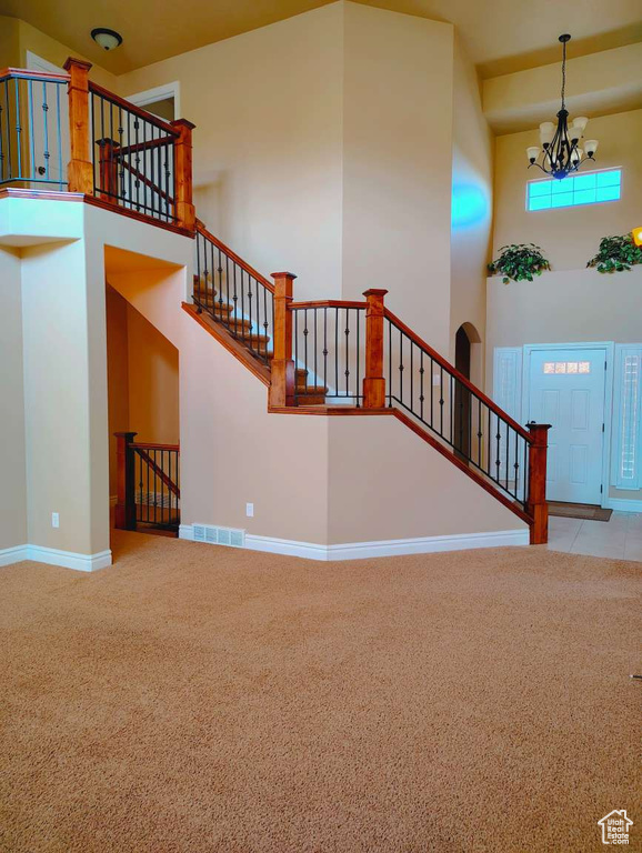 Staircase with carpet floors, a chandelier, baseboards, a towering ceiling, and visible vents