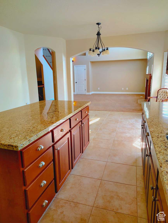 Kitchen with pendant lighting, light tile patterned flooring, reddish brown cabinets, a chandelier, and arched walkways
