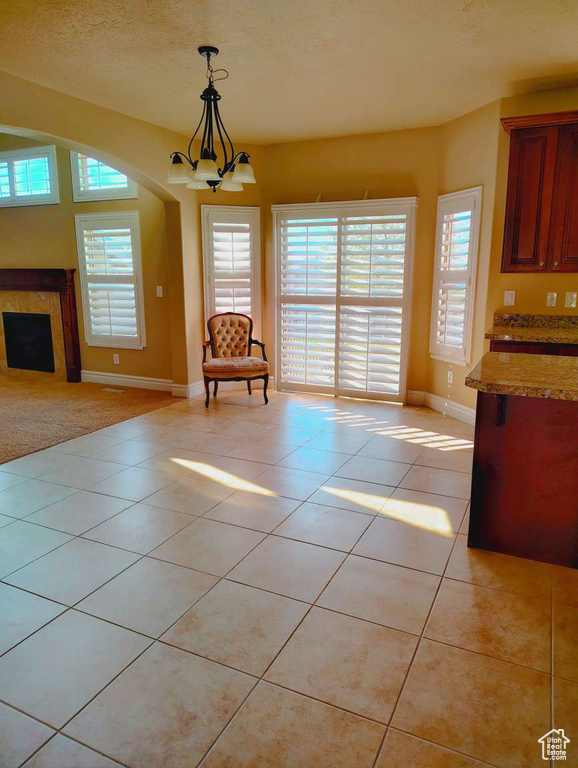 Unfurnished dining area with baseboards, a premium fireplace, light tile patterned flooring, and a notable chandelier