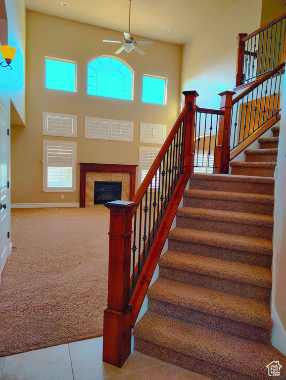 Stairs featuring a tiled fireplace, baseboards, ceiling fan, and a healthy amount of sunlight