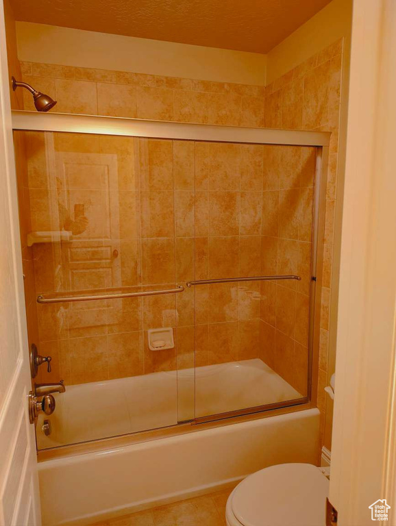 Bathroom featuring combined bath / shower with glass door, tile patterned floors, and toilet