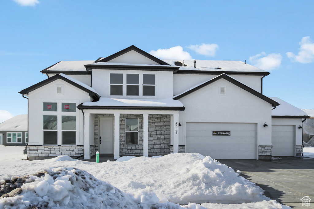 View of front facade with an attached garage, stucco siding, driveway, and stone siding