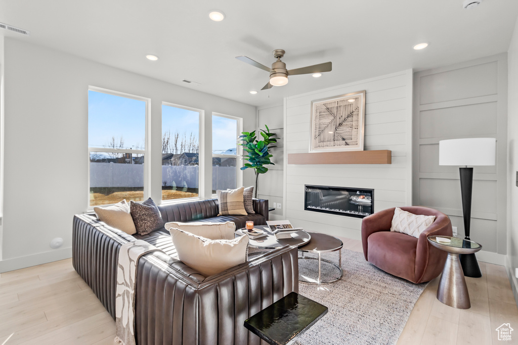 Living area with a glass covered fireplace, wood finished floors, baseboards, ceiling fan, and recessed lighting
