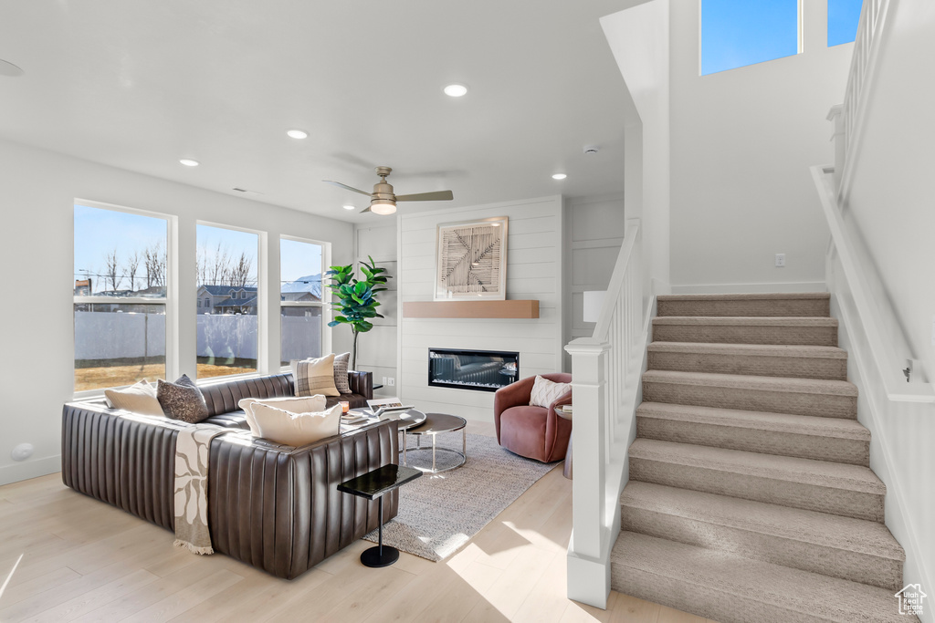 Living area featuring a ceiling fan, stairs, wood finished floors, a glass covered fireplace, and recessed lighting