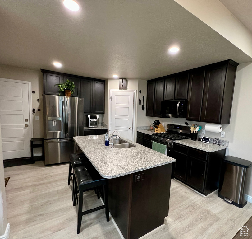 Kitchen with a sink, appliances with stainless steel finishes, a kitchen island with sink, and light wood-style flooring