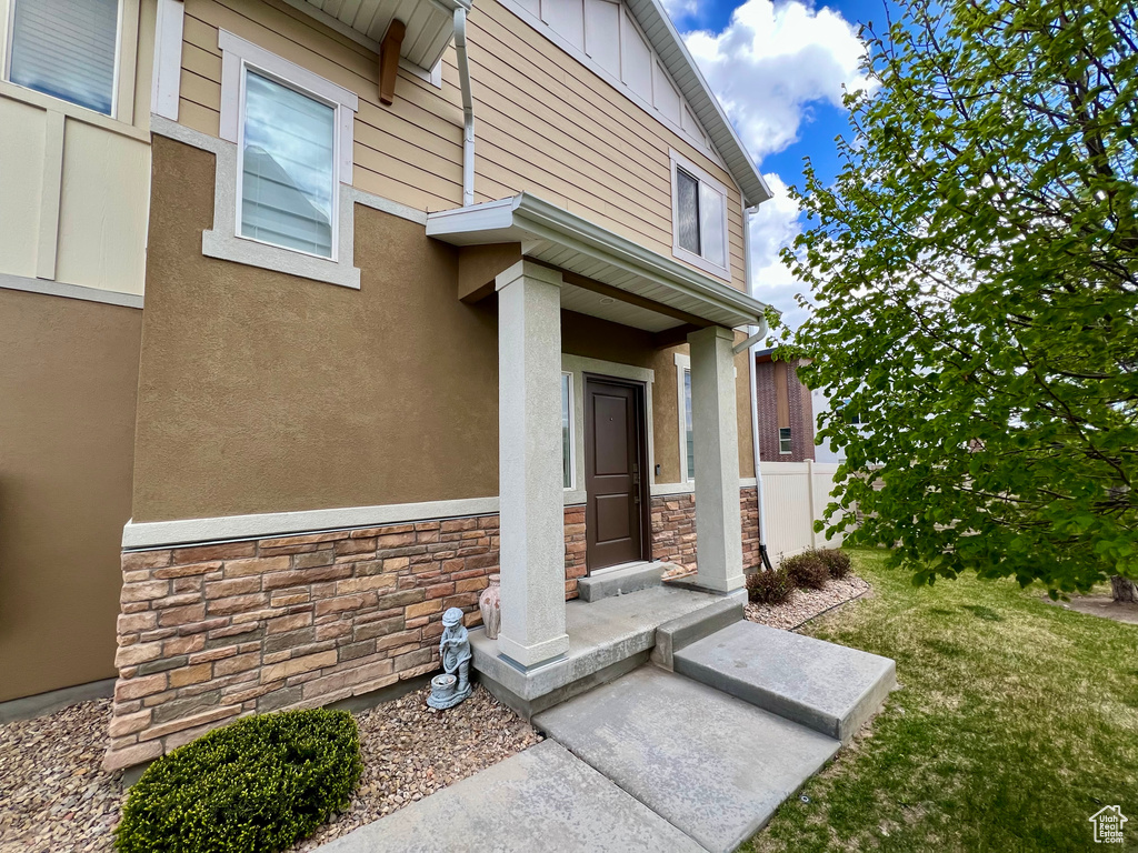 View of exterior entry featuring stucco siding, a yard, and stone siding