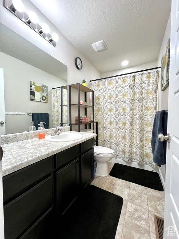 Bathroom with a textured ceiling, visible vents, vanity, tile patterned floors, and toilet
