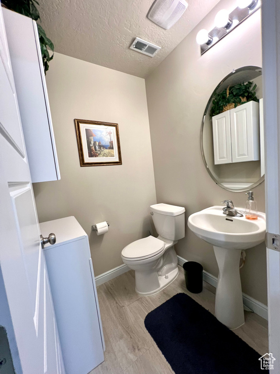 Bathroom featuring a textured ceiling, visible vents, wood finished floors, baseboards, and toilet
