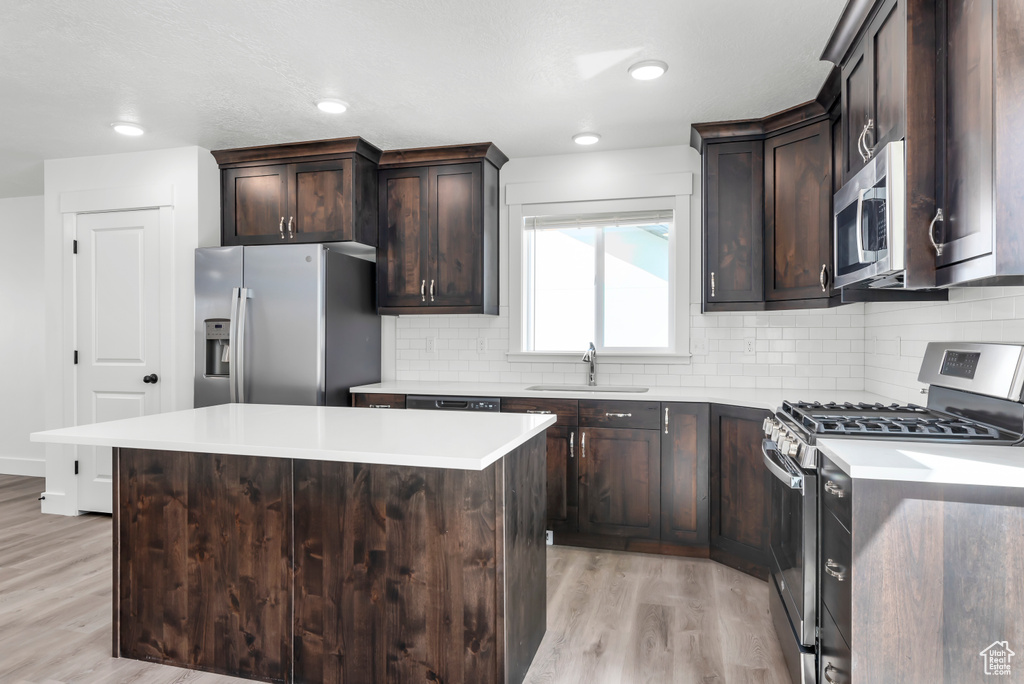 Kitchen featuring decorative backsplash, light wood-type flooring, dark brown cabinets, a sink, and stainless steel appliances