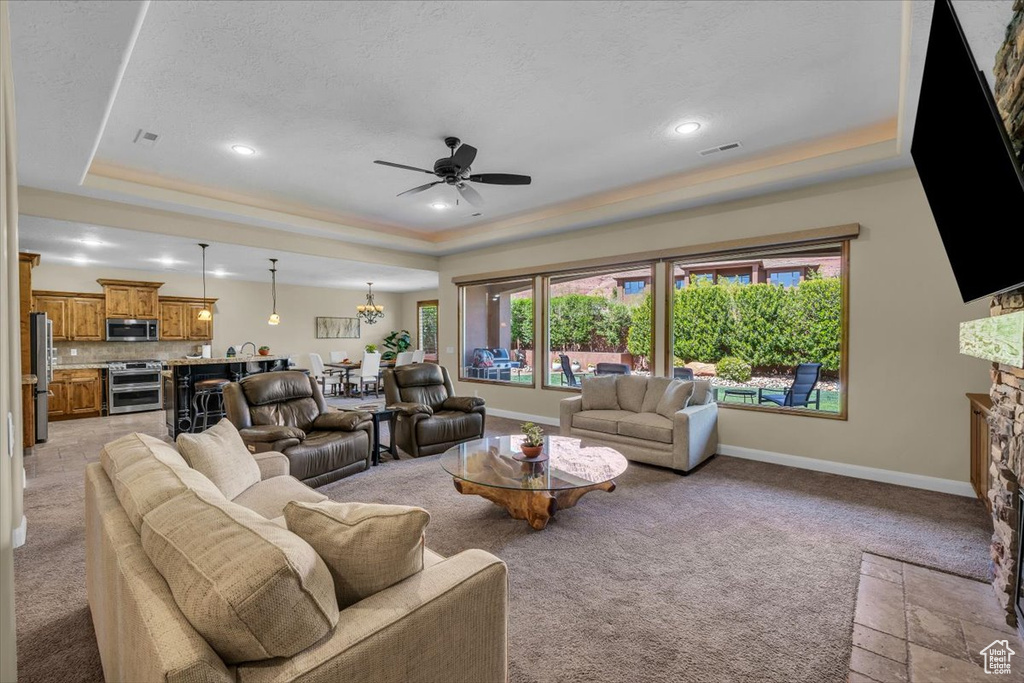 Living area with ceiling fan, light colored carpet, a stone fireplace, a tray ceiling, and visible vents