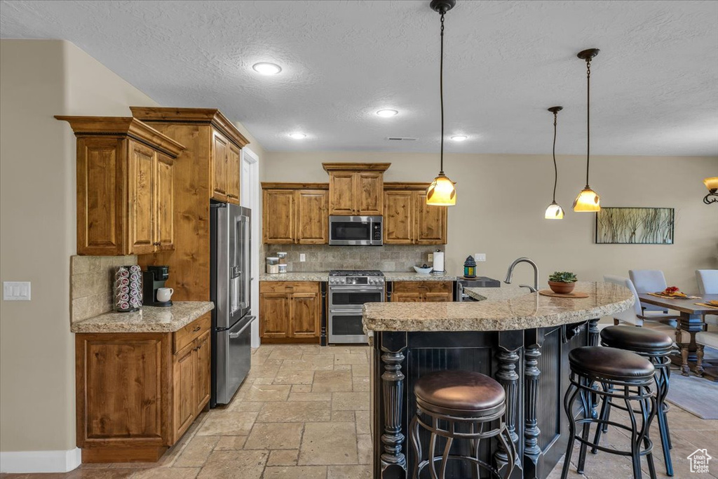Kitchen featuring brown cabinets, stainless steel appliances, a textured ceiling, and tasteful backsplash