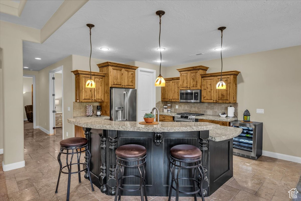 Kitchen with beverage cooler, stone tile floors, brown cabinets, and stainless steel appliances