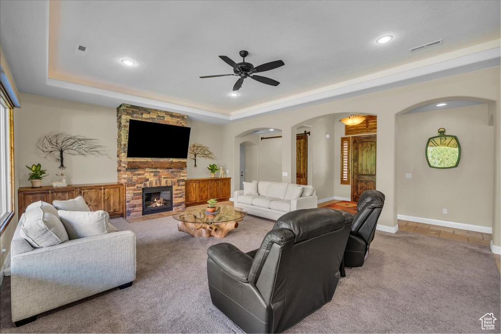Living area with visible vents, a ceiling fan, carpet flooring, a tray ceiling, and arched walkways