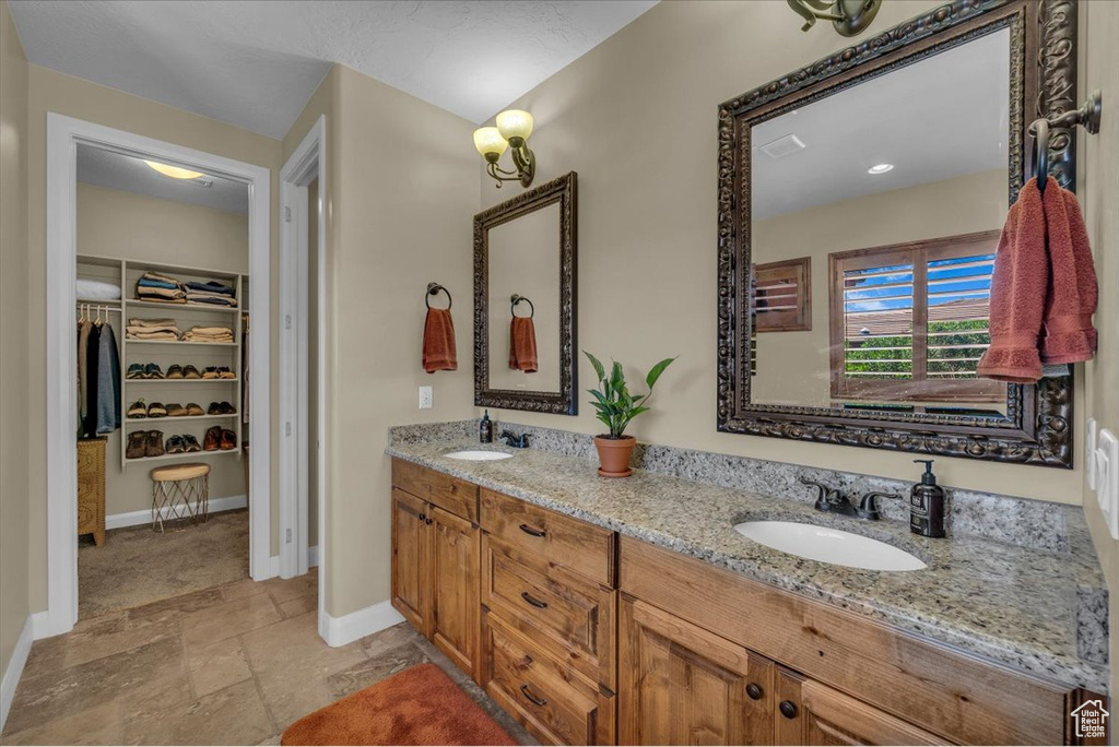 Full bath featuring double vanity, a sink, baseboards, and stone tile floors
