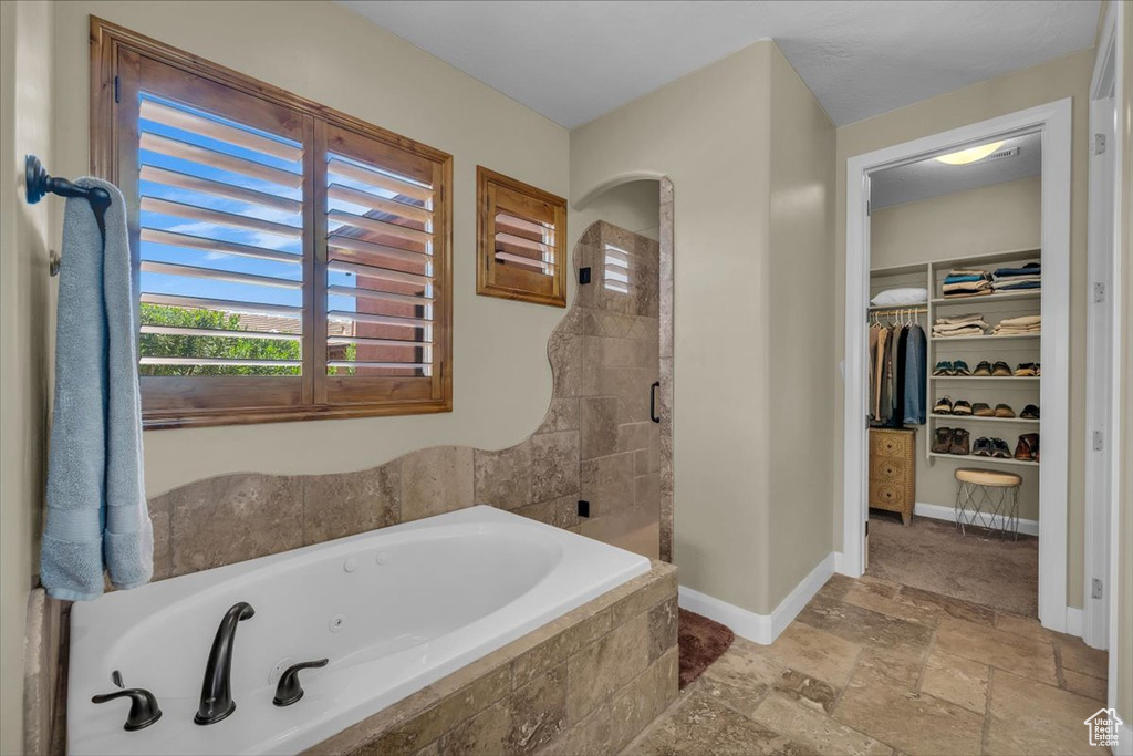 Bathroom featuring a walk in closet, a shower stall, baseboards, a whirlpool tub, and stone tile flooring
