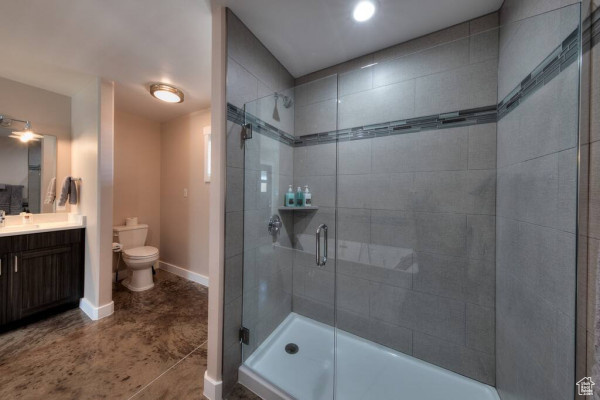 Bathroom featuring a shower stall, concrete flooring, vanity, baseboards, and toilet