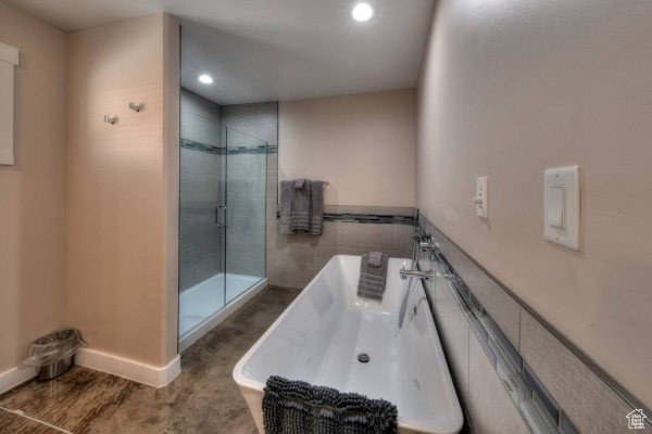 Full bath with tile walls, recessed lighting, a wainscoted wall, a soaking tub, and a stall shower