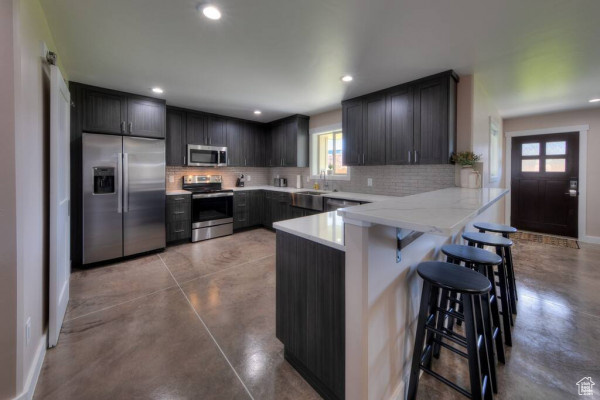 Kitchen with backsplash, stainless steel appliances, a peninsula, and finished concrete flooring