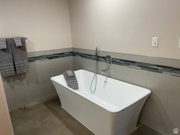 Bathroom featuring concrete flooring, tile walls, wainscoting, and a soaking tub