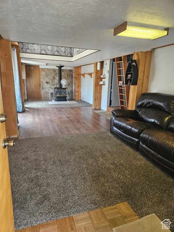 Living area with a wood stove, a textured ceiling, and wood finished floors