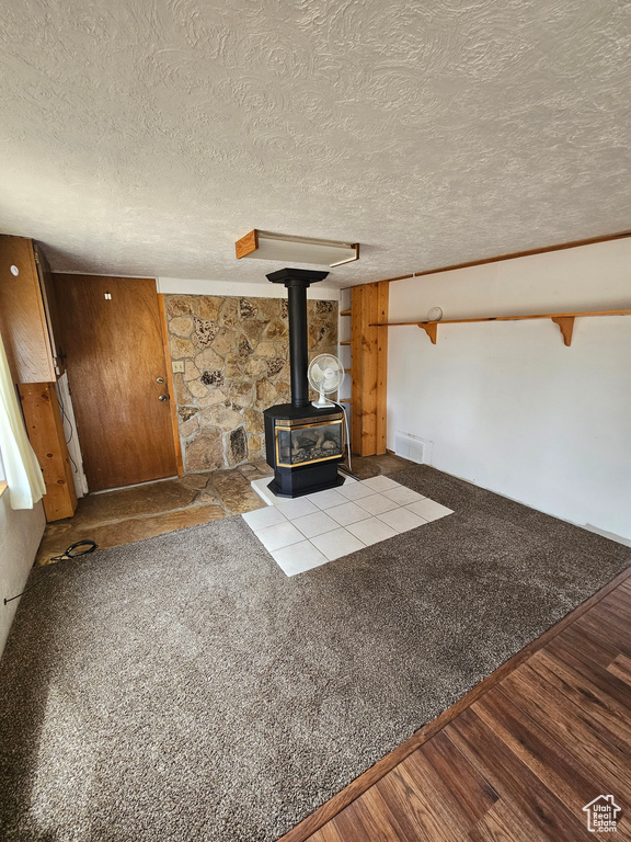 Unfurnished living room featuring a wood stove, a textured ceiling, and wood finished floors