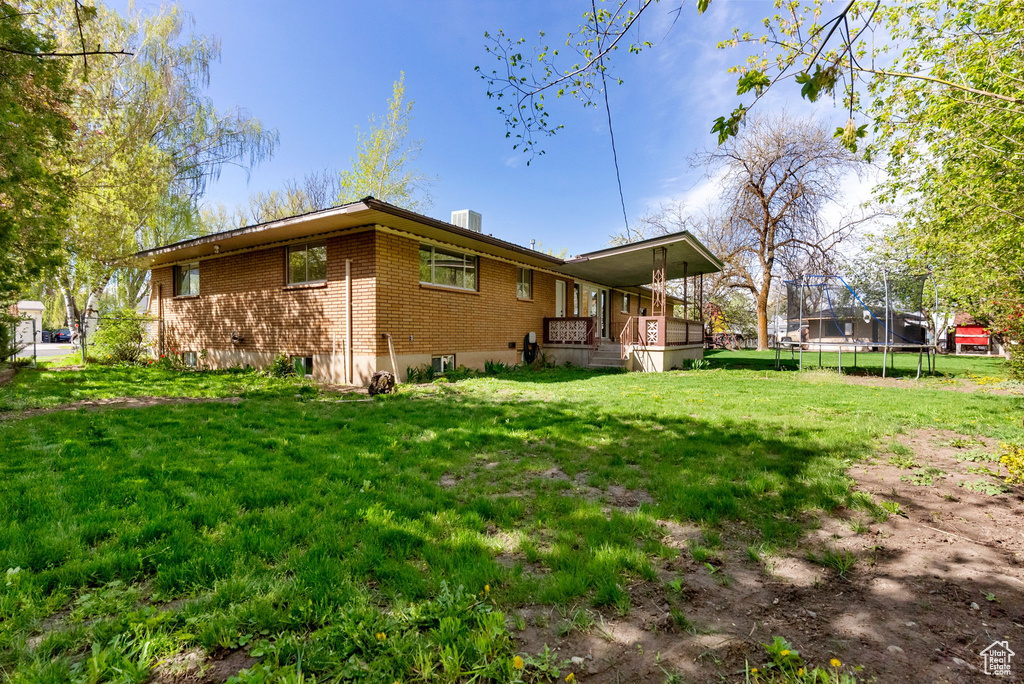 Rear view of house with central AC, brick siding, a lawn, a trampoline, and a porch