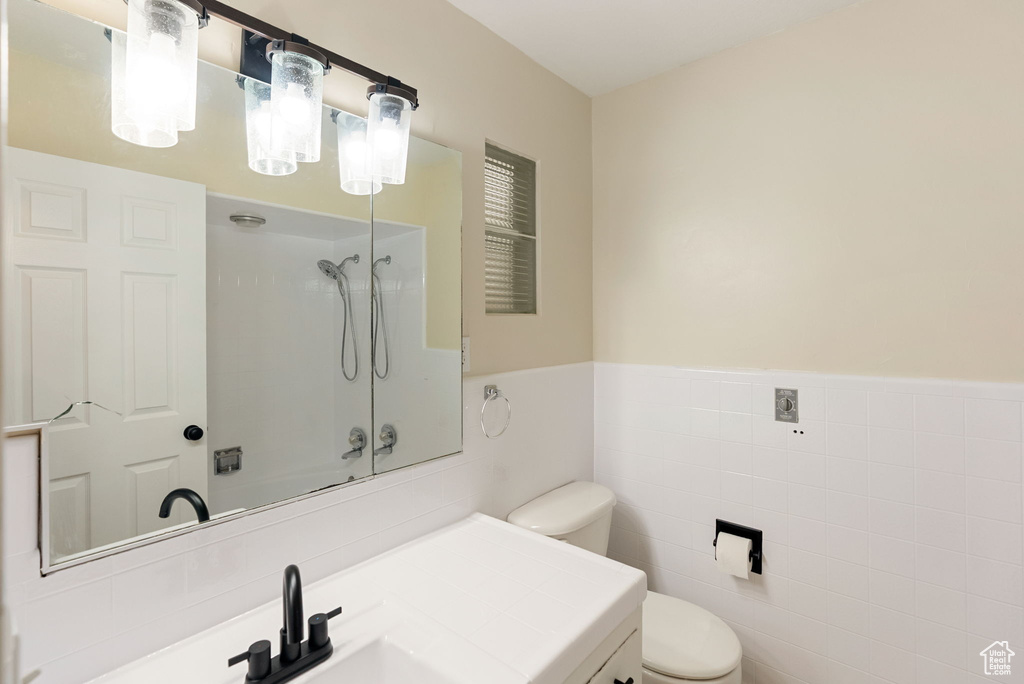 Bathroom with tile walls, wainscoting, vanity, toilet, and washtub / shower combination