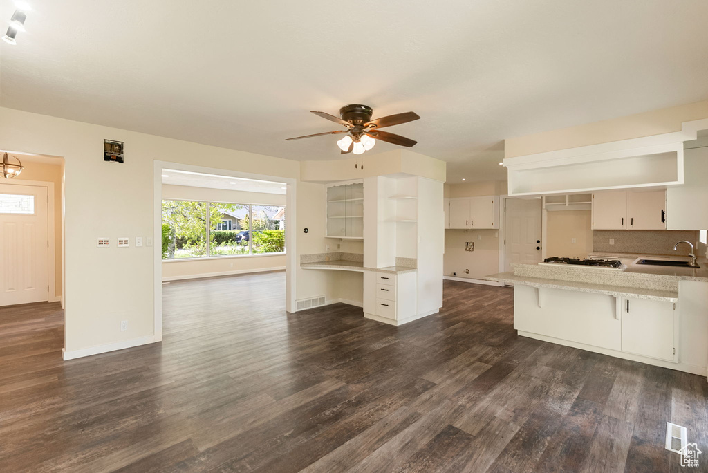 Unfurnished living room featuring visible vents, dark wood finished floors, a sink, baseboards, and ceiling fan with notable chandelier