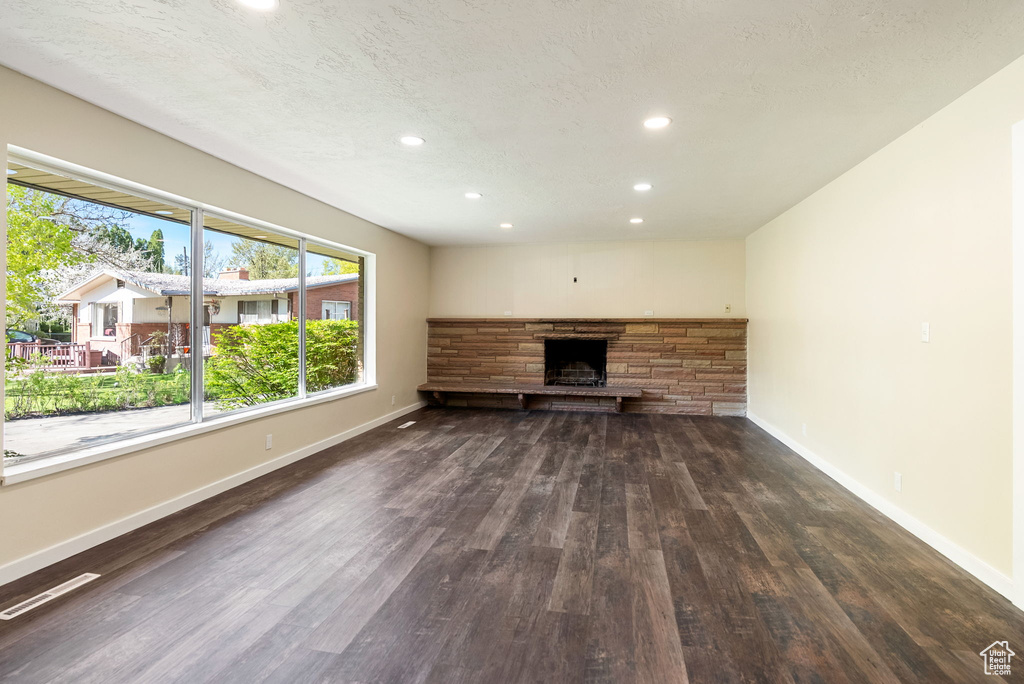 Unfurnished living room with a stone fireplace, visible vents, wood finished floors, baseboards, and recessed lighting
