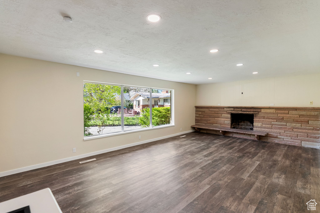 Unfurnished living room with a stone fireplace, recessed lighting, baseboards, and dark wood-type flooring