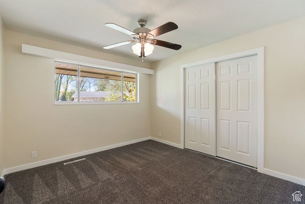 Unfurnished bedroom featuring baseboards, ceiling fan, a closet, and dark colored carpet