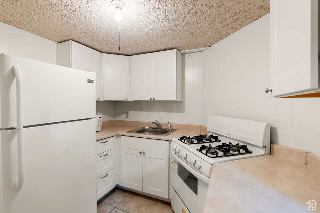 Kitchen featuring a sink, light countertops, white appliances, and white cabinetry