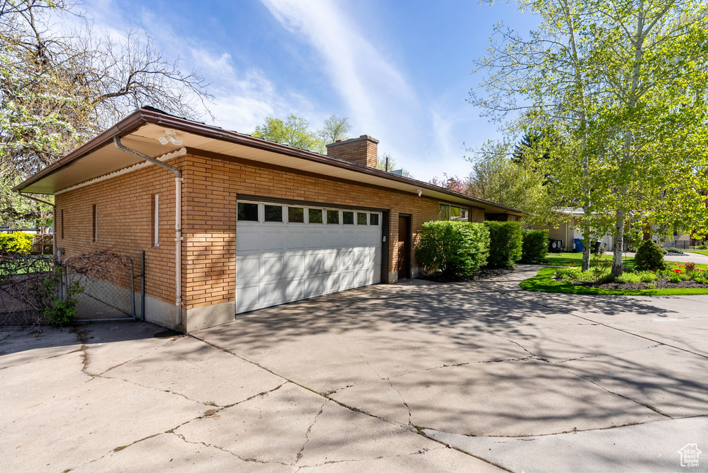 View of property exterior featuring a garage, a chimney, driveway, and brick siding