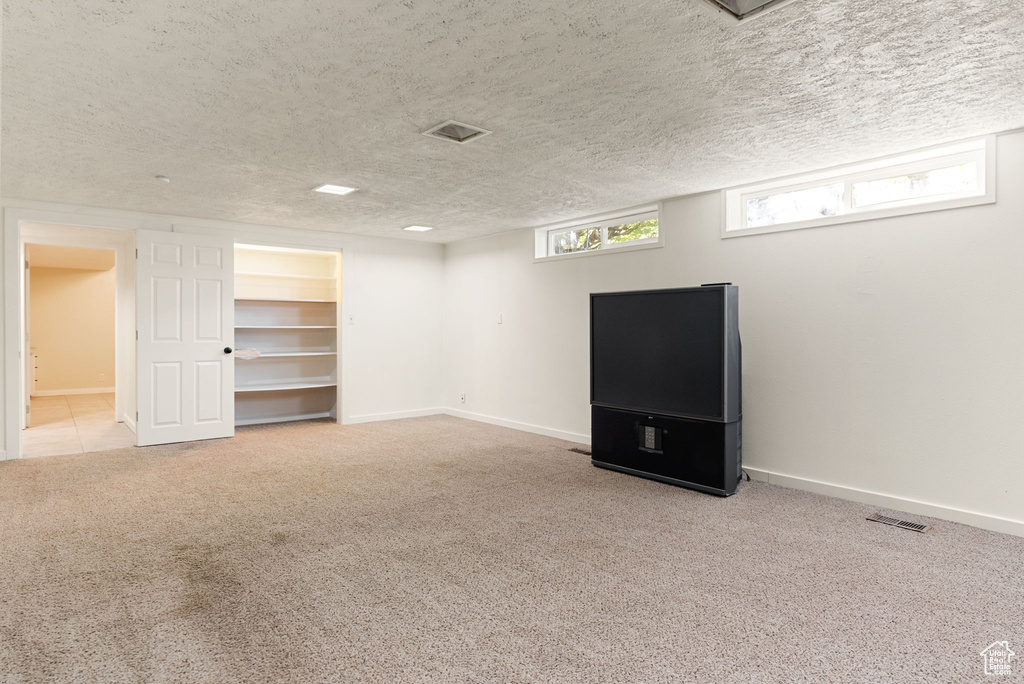 Basement featuring a textured ceiling, baseboards, visible vents, and carpet