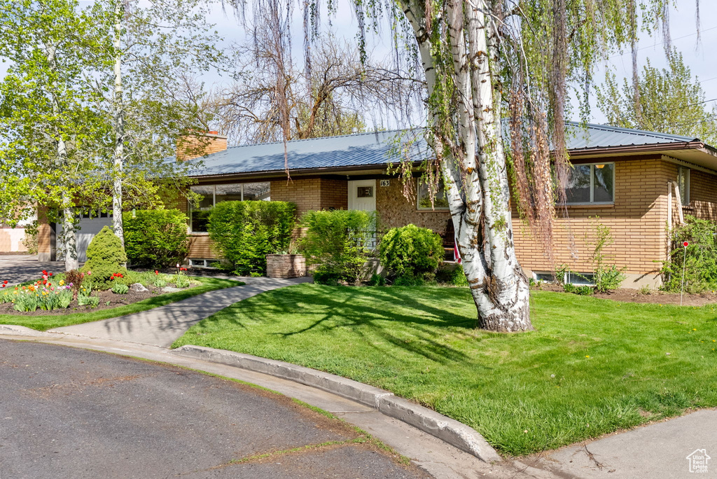 Ranch-style home with brick siding, a front yard, and metal roof